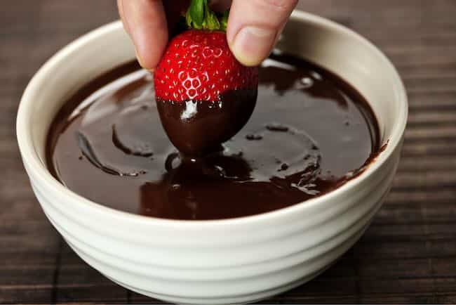dipping stawberries in bowl of tempered chocolate