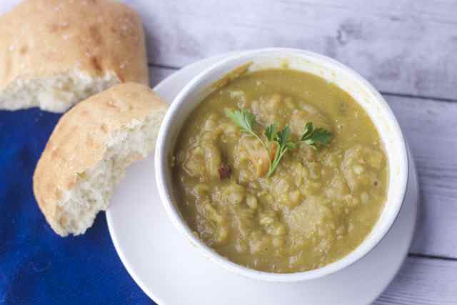 No Effort Slow Cooker Split Pea Soup Recipe in a bowl with a torn roll on blue napkin