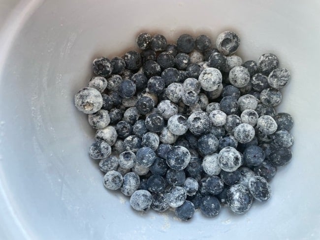 adding flour to blueberries in batter