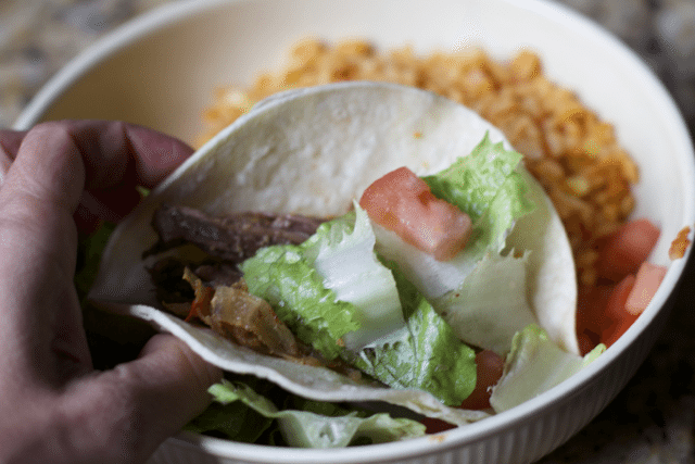 holding a finished fajita in hand over bowl of rice