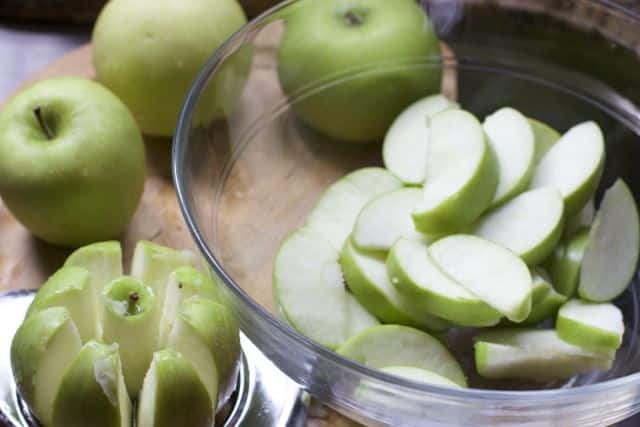 cut up granny smith apples in a bowl and one cut with an apple slicer