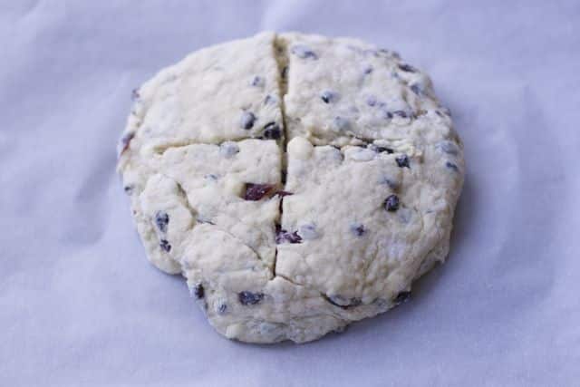 slab of irish soda bread dough in a circle with 2 slits in the middle on a piece of parchment