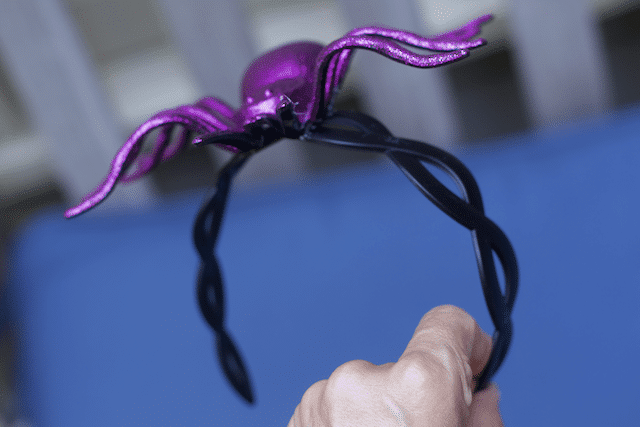 Holding up a black headband with a purple spider glued on