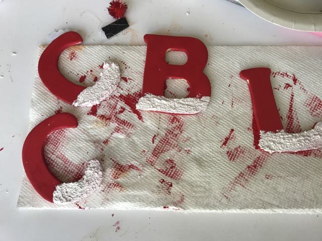 Red painted letters with bottoms painted with snow paint on dirty paper towel 