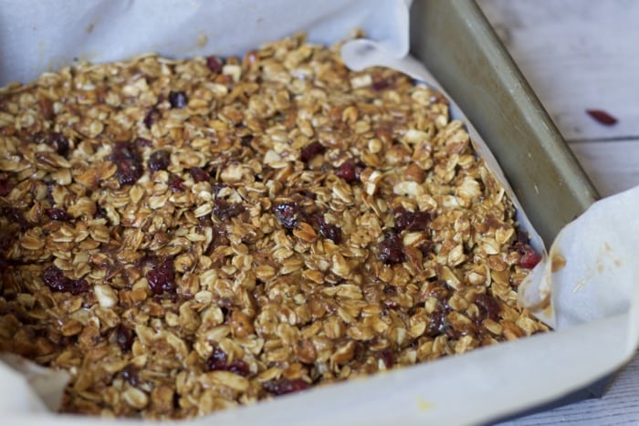 chewy granola bars pressed into a baking pan lined with parchment paper